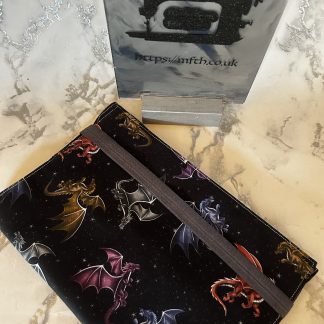Book Cover handmade from fabrics with an elasticated band to hold it together around the top. The print is black on the background with colourful dragons flying around on it