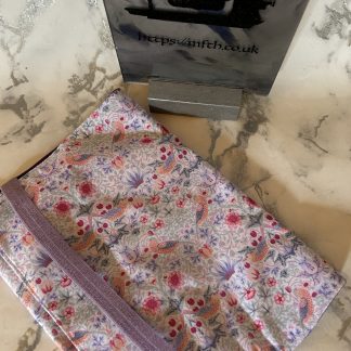 Book Cover made from several layers of fabric with an elasticated band to hold it together at the edge. The print is lilac in the background with lilac, red and white across it