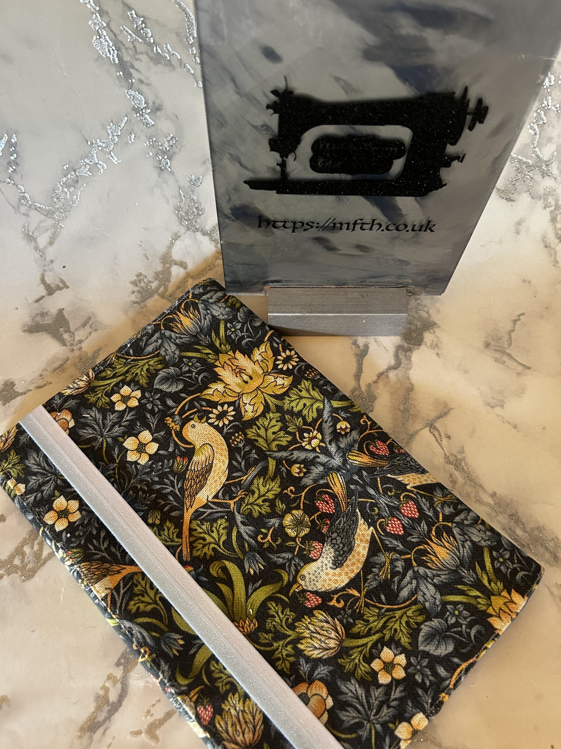 Book Cover made from several layers of fabric with an elasticated band to hold it together at the edge. The print is Navy with yellow bird and flowers in the William Morris Print