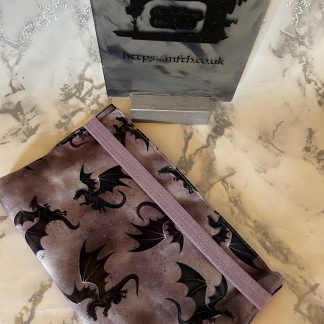 Book Cover handmade from fabrics with an elasticated band to hold it together around the top. The print is purple and grey mix on the background with colourful dragons flying around on it